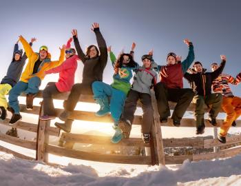 friends in ski gear sitting on a fence, arms raised in celebration