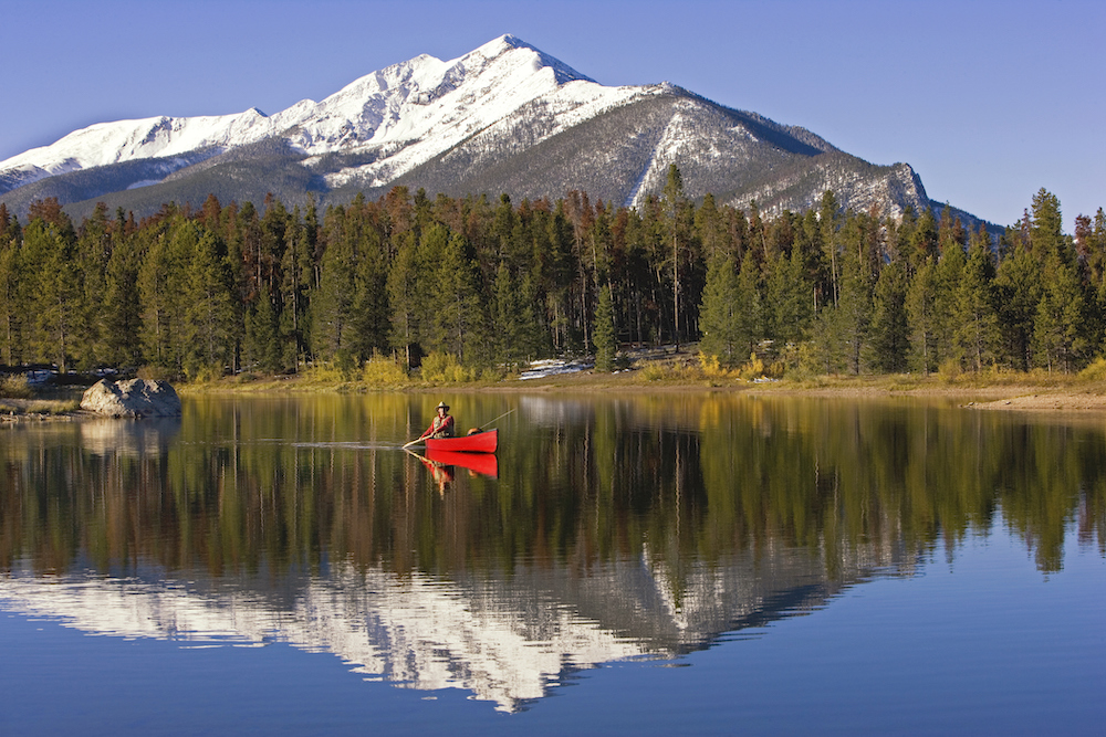 person in a red canoe on a smooth body of water with Rocky Mountains in the background