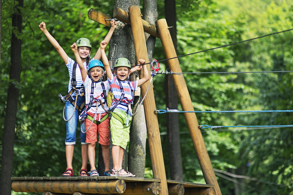 three kids standing on a platform of a ropes course 